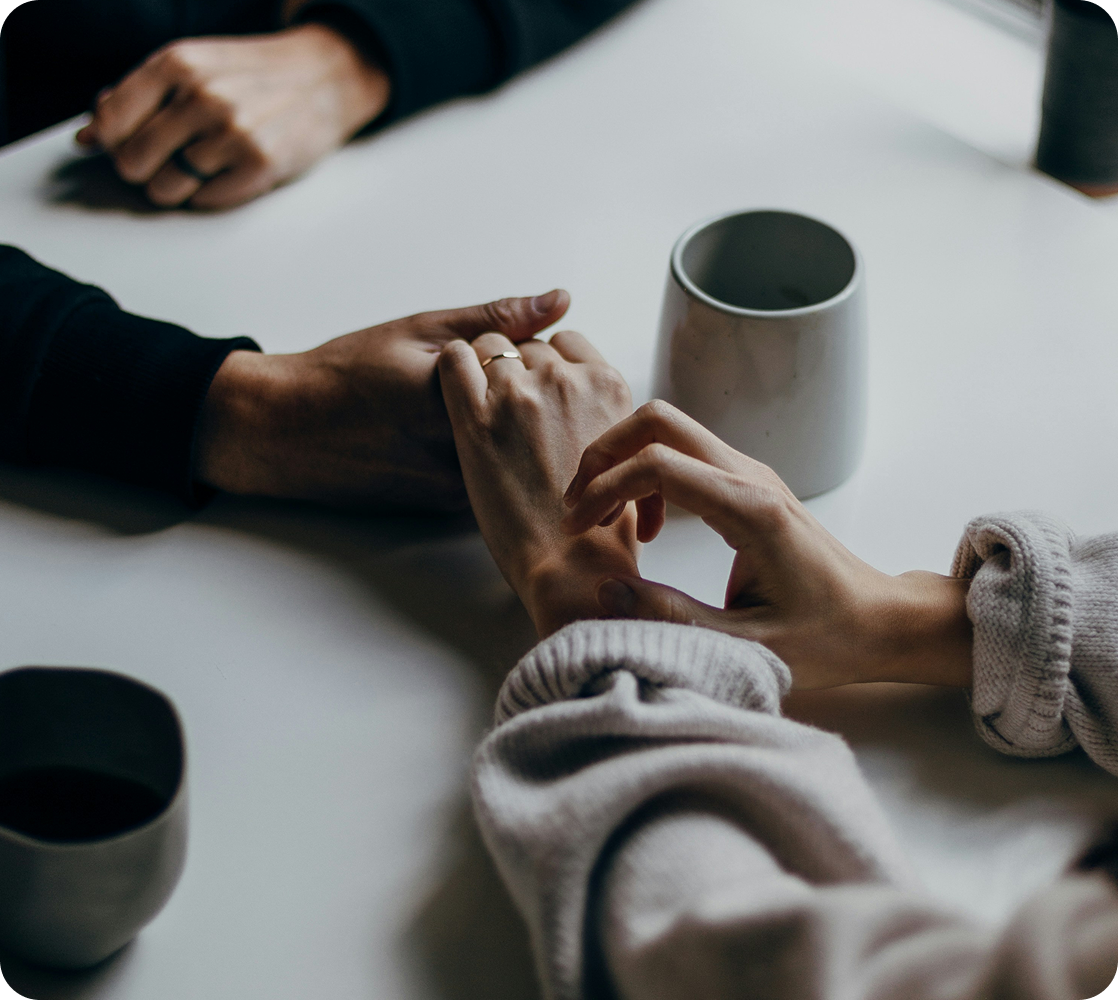 Two people holding hands across a table as they talk.